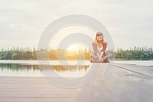 Young hipster woman sitting on pier and smiling at the camera.