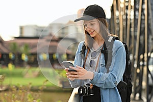 Young hipster woman traveler using mobile phone while standing on bridge over a river in the city