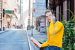 Young Hispanic American Man reading red book, talking on cell phone outside in New York City