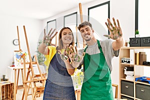 Young hispanic artist couple smiling happy showing painted palm hands at art studio