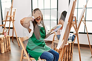 Young hispanic artist women painting on canvas at art studio surprised with hand on head for mistake, remember error
