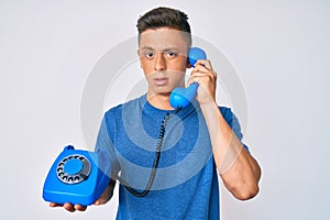 Young hispanic boy holding vintage telephone clueless and confused expression