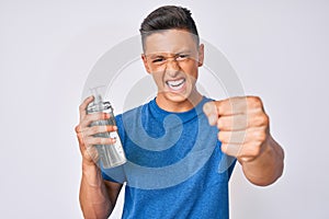 Young hispanic boy using hand sanitizer gel annoyed and frustrated shouting with anger, yelling crazy with anger and hand raised