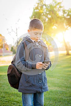 Young Hispanic Boy Walking Outdoors With Backpack Texting on Cell Phone