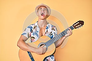 Young hispanic boy wearing summer style playing classical guitar angry and mad screaming frustrated and furious, shouting with