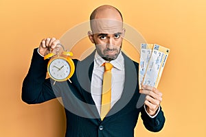 Young hispanic business man holding boarding pass and alarm clock depressed and worry for distress, crying angry and afraid