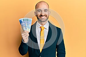 Young hispanic business man holding south african 100 rand banknotes looking positive and happy standing and smiling with a