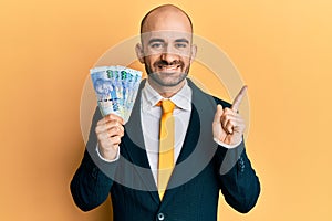 Young hispanic business man holding south african 100 rand banknotes smiling happy pointing with hand and finger to the side