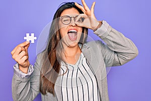 Young hispanic business woman holding puzzle peace as cooperation and union on work with happy face smiling doing ok sign with