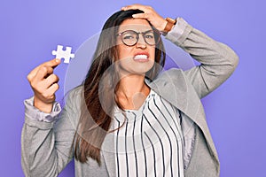 Young hispanic business woman holding puzzle peace as cooperation and union on work stressed with hand on head, shocked with shame