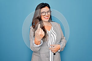 Young hispanic business woman wearing glasses standing over blue isolated background Beckoning come here gesture with hand