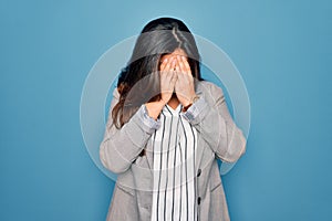 Young hispanic business woman wearing glasses standing over blue isolated background with sad expression covering face with hands