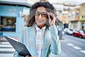 Young hispanic business woman wearing professional look smiling confident at the city holding worker clipboard