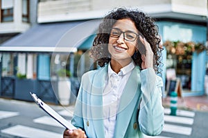 Young hispanic business woman wearing professional look smiling confident at the city holding worker clipboard