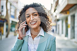 Young hispanic business woman wearing professional look smiling confident at the city speaking on the phone