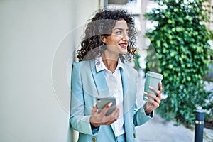 Young hispanic business woman wearing professional look smiling confident at the city using smartphone