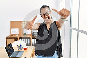 Young hispanic business woman working at the office approving doing positive gesture with hand, thumbs up smiling and happy for