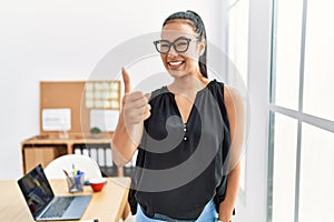 Young hispanic business woman working at the office doing happy thumbs up gesture with hand