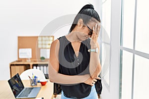 Young hispanic business woman working at the office with sad expression covering face with hands while crying