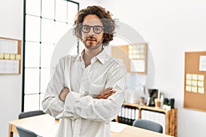 Young hispanic businessman with serious expression standing with arms crossed gesture at office