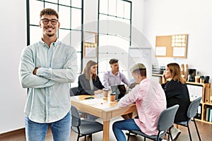Young hispanic businessman smiling happy standing with arms crossed gesture at the office during business meeting