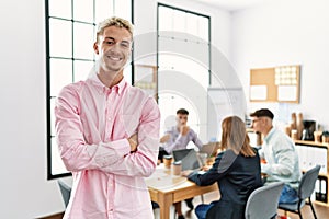 Young hispanic businessman smiling happy standing with arms crossed gesture at the office during business meeting