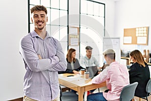 Young hispanic businessman smiling happy standing with arms crossed gesture at the office during business meeting