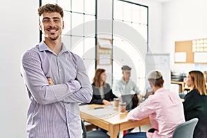 Young hispanic businessman smiling happy standing with arms crossed gesture at the office during business meeting