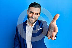 Young hispanic businessman wearing business jacket smiling friendly offering handshake as greeting and welcoming