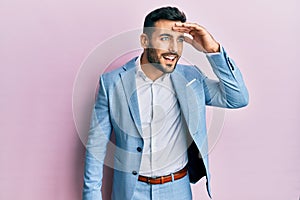 Young hispanic businessman wearing business jacket very happy and smiling looking far away with hand over head