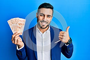 Young hispanic businessman wearing business suit holding turkish lira banknotes smiling happy and positive, thumb up doing