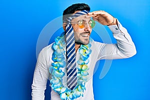 Young hispanic businessman wearing party funny style with tie on head very happy and smiling looking far away with hand over head