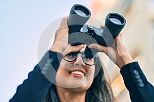 Young hispanic businesswoman looking for new opportunity using binoculars at the city