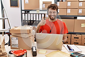 Young hispanic call center agent man working at warehouse doing happy thumbs up gesture with hand