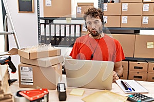 Young hispanic call center agent man working at warehouse making fish face with lips, crazy and comical gesture