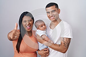 Young hispanic couple with baby standing together over isolated background approving doing positive gesture with hand, thumbs up