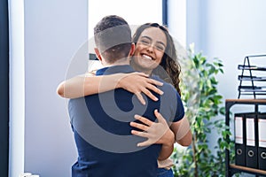 Young hispanic couple business workers hugging each other standing at office