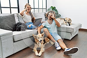 Young hispanic couple with dogs relaxing at home doing ok gesture with hand smiling, eye looking through fingers with happy face