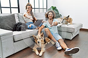 Young hispanic couple with dogs relaxing at home smiling cheerful offering palm hand giving assistance and acceptance