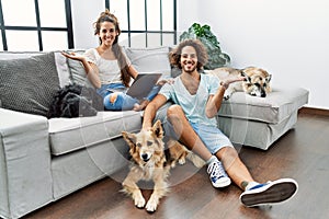 Young hispanic couple with dogs relaxing at home smiling cheerful presenting and pointing with palm of hand looking at the camera