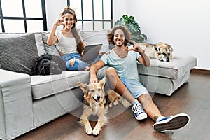 Young hispanic couple with dogs relaxing at home smiling and confident gesturing with hand doing small size sign with fingers