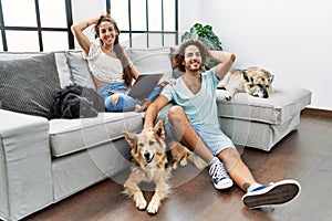 Young hispanic couple with dogs relaxing at home smiling confident touching hair with hand up gesture, posing attractive and
