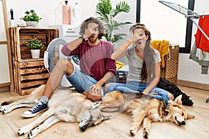 Young hispanic couple doing laundry with dogs peeking in shock covering face and eyes with hand, looking through fingers with