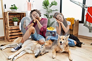 Young hispanic couple doing laundry with dogs sleeping tired dreaming and posing with hands together while smiling with closed