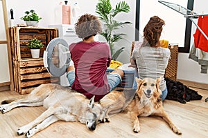 Young hispanic couple doing laundry with dogs standing backwards looking away with crossed arms