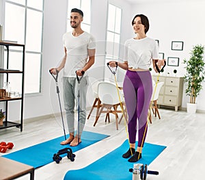 Young hispanic couple doing strong exercise using elastic band at home