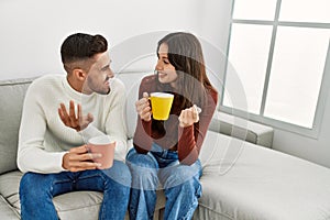 Young hispanic couple drinking coffee sitting on the sofa at home