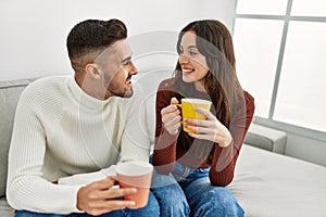 Young hispanic couple drinking coffee sitting on the sofa at home