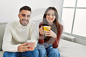 Young hispanic couple drinking coffee sitting on the sofa at home