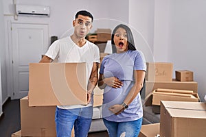 Young hispanic couple expecting a baby moving to a new home afraid and shocked with surprise and amazed expression, fear and